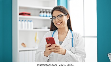 Young beautiful hispanic woman doctor using smartphone smiling at clinic - Powered by Shutterstock