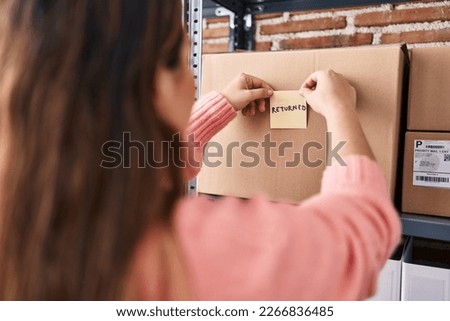 Young beautiful hispanic woman ecommerce business worker putting returned reminder paper on package at office