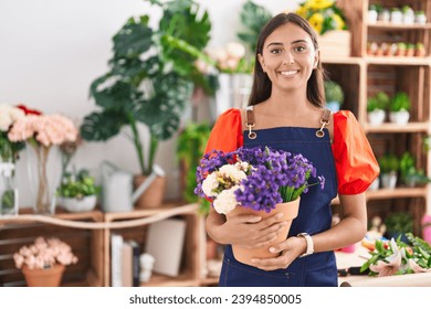 Young beautiful hispanic woman florist smiling confident holding plant at florist - Powered by Shutterstock