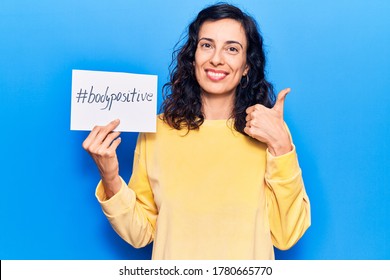 Young Beautiful Hispanic Woman Holding Paper With Hashtag Body Positive Smiling Happy And Positive, Thumb Up Doing Excellent And Approval Sign 