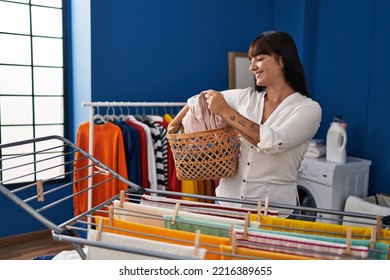 Young Beautiful Hispanic Woman Holding Wicker Basket Hanging Clothes On Clothesline At Laundry Room