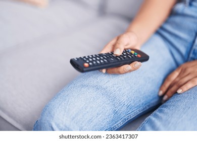 Young beautiful hispanic woman holding tv remote control sitting on sofa at home - Shutterstock ID 2363417307