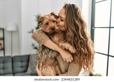 Young beautiful hispanic woman kissing and hugging dog standing at home - Powered by Shutterstock