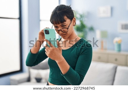 Young beautiful hispanic woman looking screen smartphone with vision problem at home