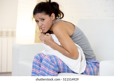 Young Beautiful Hispanic Woman In Painful Expression Holding Pillow Against Her Belly Suffering Menstrual Period Pain Lying Sad On Home Couch Having Tummy Cramp In Female Health Concept