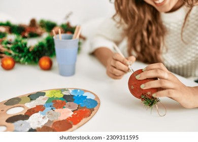 Young beautiful hispanic woman painting christmas ball sitting on table at home