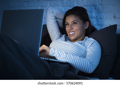 Young Beautiful Hispanic Woman In Pajamas On Bed At Home Bedroom Working Happy With Laptop Computer Late At Night Or Using The Internet Chat And Social Network In Technology Addiction Concept