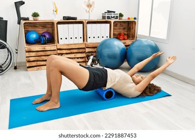 Young beautiful hispanic woman patient having rehab using foam roller at rehab clinic - Powered by Shutterstock