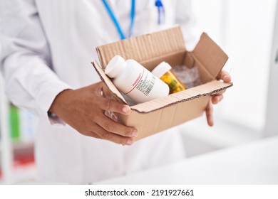 Young Beautiful Hispanic Woman Pharmacist Holding Cardboard Box With Pills Bottles At Pharmacy