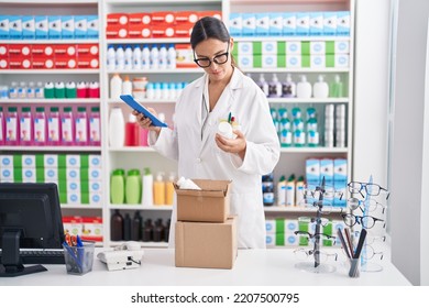 Young Beautiful Hispanic Woman Pharmacist Using Touchpad Holding Pills Bottle At Pharmacy