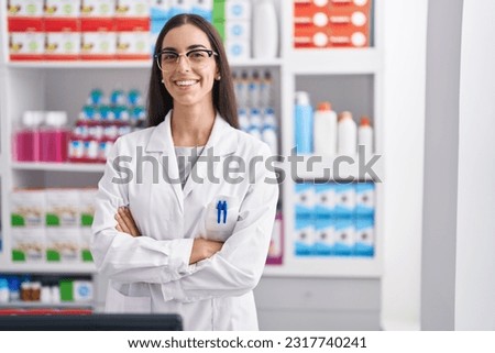 Young beautiful hispanic woman pharmacist smiling confident standing with arms crossed gesture at pharmacy