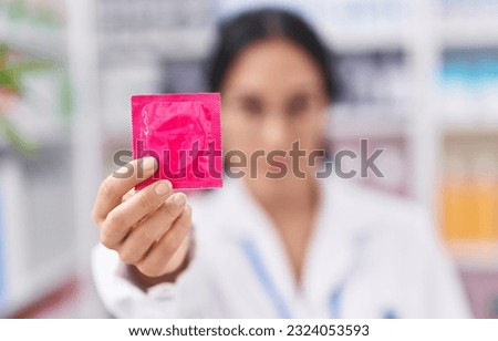 Young beautiful hispanic woman pharmacist holding condom at pharmacy