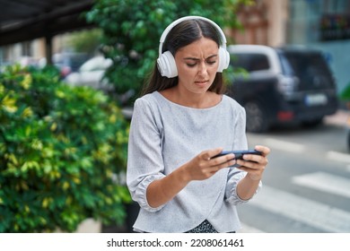 Young Beautiful Hispanic Woman Playing Video Game With Serious Expression At Street