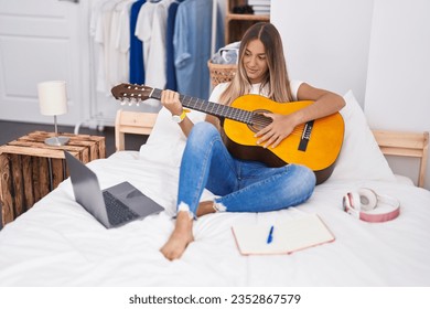 Young beautiful hispanic woman playing classical guitar sitting on bed at bedroom - Powered by Shutterstock