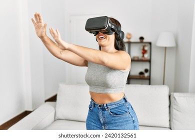 Young beautiful hispanic woman playing video game using virtual reality glasses at home - Powered by Shutterstock