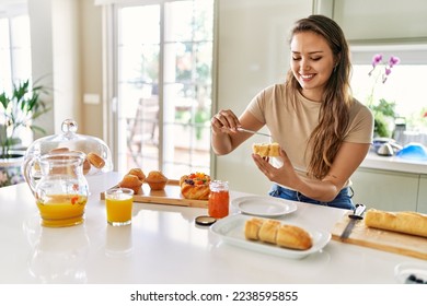 Young beautiful hispanic woman preparing breakfast putting jam on bread at the kitchen - Shutterstock ID 2238595855