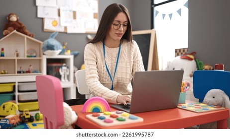 Young beautiful hispanic woman preschool teacher using laptop sitting on table at kindergarten - Shutterstock ID 2261995787