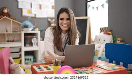 Young beautiful hispanic woman preschool teacher using laptop at kindergarten - Shutterstock ID 2327169525