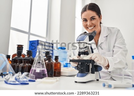 Young beautiful hispanic woman scientist smiling confident using microscope at laboratory