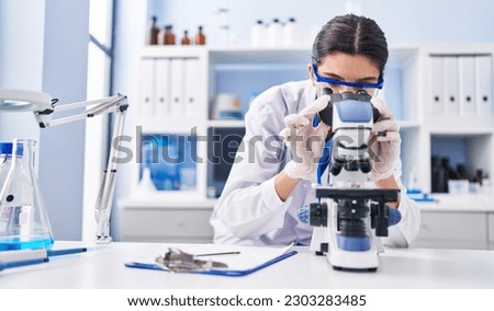 Young beautiful hispanic woman scientist using microscope at laboratory