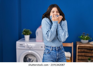 Young Beautiful Hispanic Woman Smelling Sweater Standing At Laundry Room