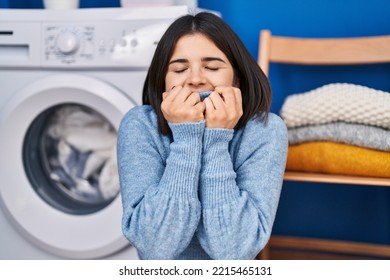 Young Beautiful Hispanic Woman Smelling Sweater Standing At Laundry Room