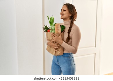 Young beautiful hispanic woman smiling confident holding groceries bag at home - Powered by Shutterstock