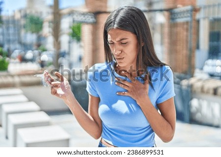 Young beautiful hispanic woman smoking and coughing at street