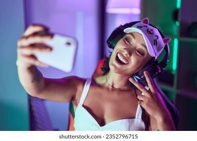 Young beautiful hispanic woman streamer smiling confident make selfie by smartphone at gaming room