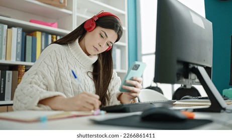 Young beautiful hispanic woman student writing on notebook using smartphone studying at university classroom - Powered by Shutterstock