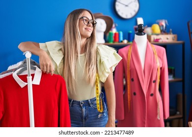 Young Beautiful Hispanic Woman Tailor Smiling Confident Leaning On Clothes Rack At Clothing Factory