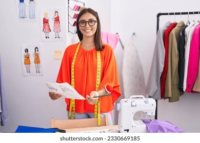 Young beautiful hispanic woman tailor smiling confident looking clothing design at tailor shop - Powered by Shutterstock