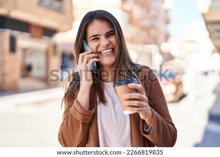 Young beautiful hispanic woman talking on smartphone drinking coffee at street