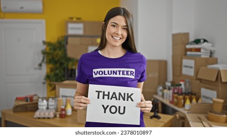 Young beautiful hispanic woman volunteer holding thank you message smiling at charity center
