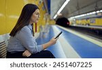 Young beautiful hispanic woman waiting for the subway using smartphone in subway station of Madrid