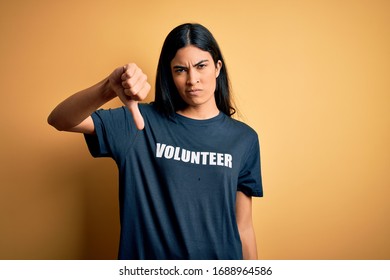 Young Beautiful Hispanic Woman Wearing Volunteer T-shirt As Social Charity Moral Looking Unhappy And Angry Showing Rejection And Negative With Thumbs Down Gesture. Bad Expression.