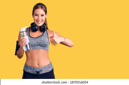 Young beautiful hispanic woman wearing sportswear holding water bottle smiling happy and positive, thumb up doing excellent and approval sign 