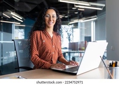 Young beautiful hispanic woman working inside modern office, businesswoman smiling and looking at camera at work using laptop. - Powered by Shutterstock