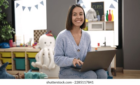 Young beautiful hispanic woman working as a teacher using laptop at kindergarten - Powered by Shutterstock