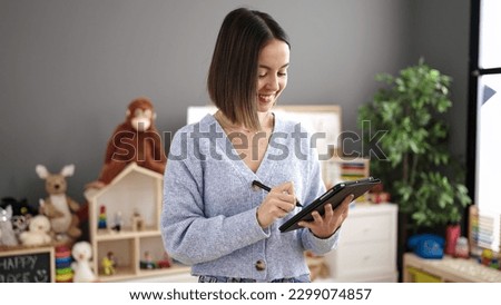 Young beautiful hispanic woman working as a teacher using touchpad at kindergarten