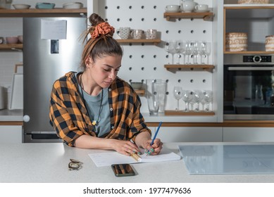 Young Beautiful House Wife And Business Owner Of Catering Company Standing In The Kitchen Writing Recipes For New Food She Want To Offer To The Clients