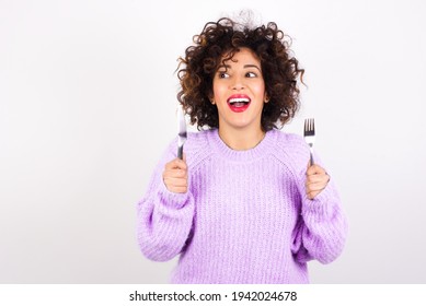 young beautiful hungry woman wearing pink knitted sweater against white background holding in hand fork knife want tasty yummy pizza, pasta and apple pie
