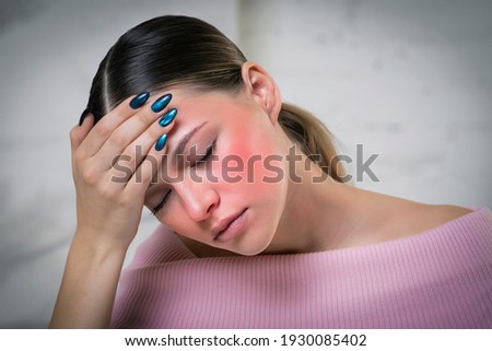 Young beautiful ill sick woman is suffering from heat, high temperature, headache and migraine, holding hand on forehead. Symptoms of the coronavirus, covid-19. Dangerous sunburn. Red face, blushing.