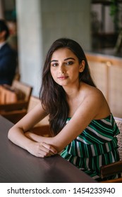 A Young And Beautiful Indian Asian Woman Sits For Her Portrait Head Shot In A Stylish Cafe During The Day. She Projects Confidence And She Looks Like She Belongs In High Society. 