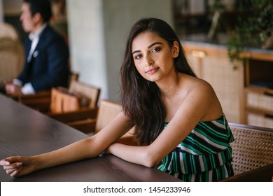 A Young And Beautiful Indian Asian Woman Sits For Her Portrait Head Shot In A Stylish Cafe During The Day. She Projects Confidence And She Looks Like She Belongs In High Society. 