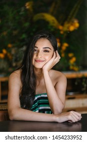 A Young And Beautiful Indian Asian Woman Sits For Her Portrait Head Shot In A Stylish Cafe During The Day. She Projects Confidence And She Looks Like She Belongs In High Society. 