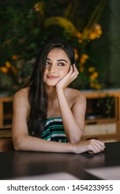 A Young And Beautiful Indian Asian Woman Sits For Her Portrait Head Shot In A Stylish Cafe During The Day. She Projects Confidence And She Looks Like She Belongs In High Society. 