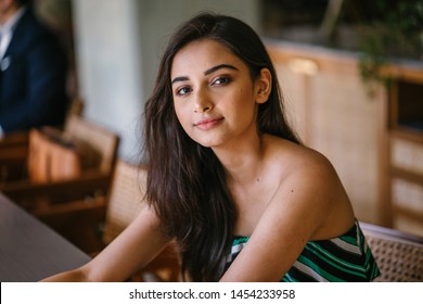 A Young And Beautiful Indian Asian Woman Sits For Her Portrait Head Shot In A Stylish Cafe During The Day. She Projects Confidence And She Looks Like She Belongs In High Society. 