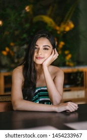 A Young And Beautiful Indian Asian Woman Sits For Her Portrait Head Shot In A Stylish Cafe During The Day. She Projects Confidence And She Looks Like She Belongs In High Society. 