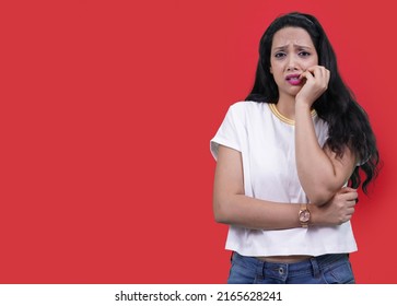 Young Beautiful Indian Girl Or Young South Asian Woman, Nervous And Bites Nails, Studio Photo Isolated On A Orange Background. Woman With Guilty Expression. Poor Woman Did Mistake Expression.